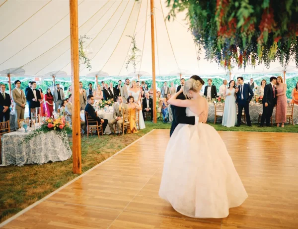 Daytime interior Sperry sailcloth tent with center pole and greenery decor. Bride and groom on dance floor.