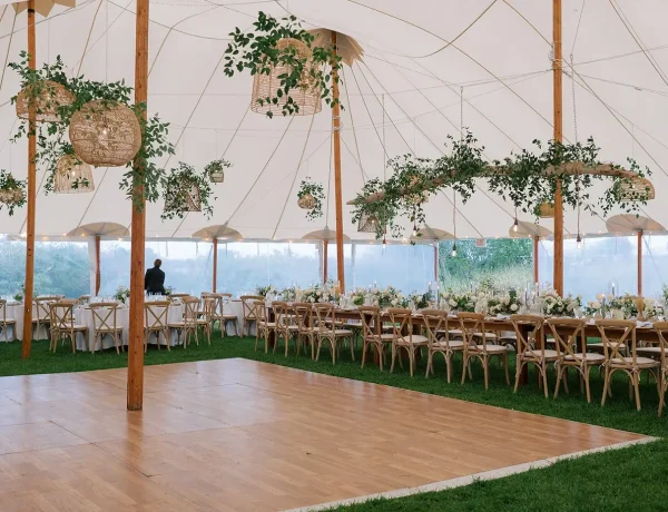 Daytime interior Sperry sailcloth tent with center pole and greenery decor. and dance floor.